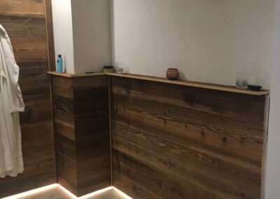 Rechte Seite des Badezimmers mit Fokus auf den Übergang zwischen Altholz-Wand und grauer Fliesenoptik.