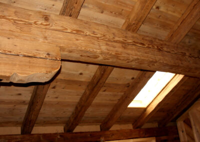 Dachbodenausbau mit sichtbaren handgehackten Altholz-Sparren, passender Dachschalung und einem modernen Dachfenster für natürlichen Lichteinfall.