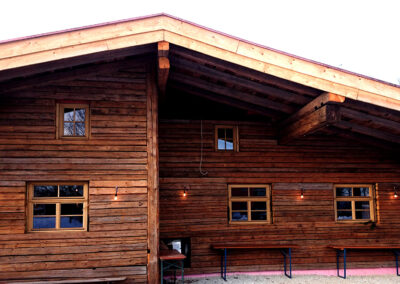 Frontansicht eines Hauses mit einer Fassadenverkleidung aus handgehackten Altholz-Sparren in authentischer Blockbau-Optik.