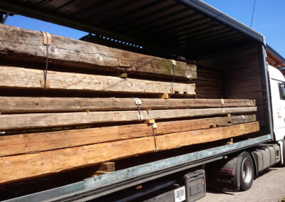 Ein voll beladener LKW mit Altholz-Kantholz im Rohzustand, der die beeindruckenden Querschnitte und die ursprüngliche Patina der historischen Balken zeigt.