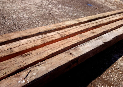 Schräge Ansicht von vier unbehandelten, handgehackten Altholz-Sparren, die die ursprüngliche Patina und die rohen Axtschläge in ihrer gesamten Länge zeigen.