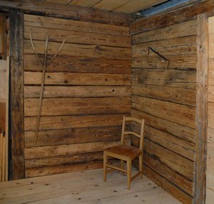 Rustikaler Innenraum mit zwei Wänden aus handgehackten Altholzbrettern, dekoriert mit einer antiken Heugabel und einer alten Handsäge.