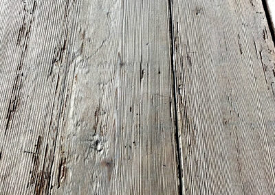 Nahaufnahme eines verlegten Altholzbodens, der die aufbereitete Oberfläche mit ihrer schönen, tiefen Struktur und die Maserung der einzelnen Dielen im Detail zeigt.