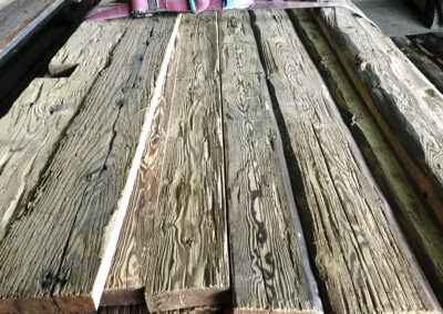 Detailaufnahme eines Stapels Altholzbretter mit traditionell handgehackter Oberflächenstruktur und historischer Patina.