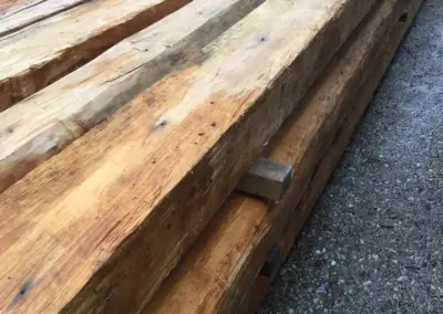 Detailaufnahme eines Stapels extrem langer Altholz-Kanthölzer, die die beeindruckende Spannweite und Geradlinigkeit der historischen Balken betont.