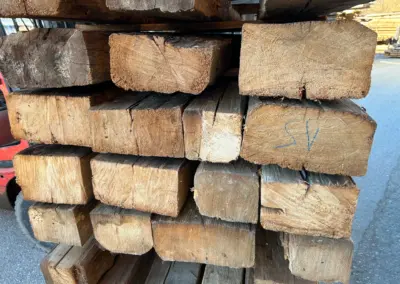 Seitliche Ansicht eines Stapels massiver Altholz-Blockbohlen, die die charakteristischen Querschnitte, Jahresringe und die Tiefe des historischen Holzes zeigen.