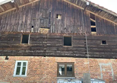 Außenansicht eines historischen Gebäudes mit sonnenverbrannter Altholz-Blockwand vor dem fachgerechten Abbau und der Bergung des Materials.