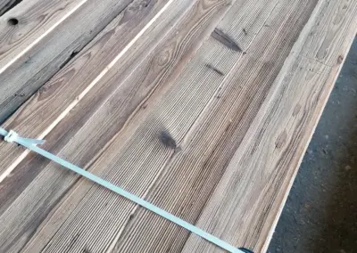 Detailansicht eines gebündelten Stapels hochwertig gebürsteter Altholzbretter mit markanter brauner Patina.