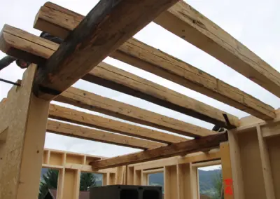 Blick von unten nach oben auf montierte Altholz-Kanthölzer als Decken-Sparren im ersten Geschoss eines Rohbaus vor grauem Himmel.