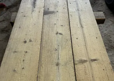 Detailansicht von oben auf einen Stapel Altholz-Bodenbretter, die die tiefe, kräftige Oberflächenstruktur und die natürliche Breite der Dielen zeigt.