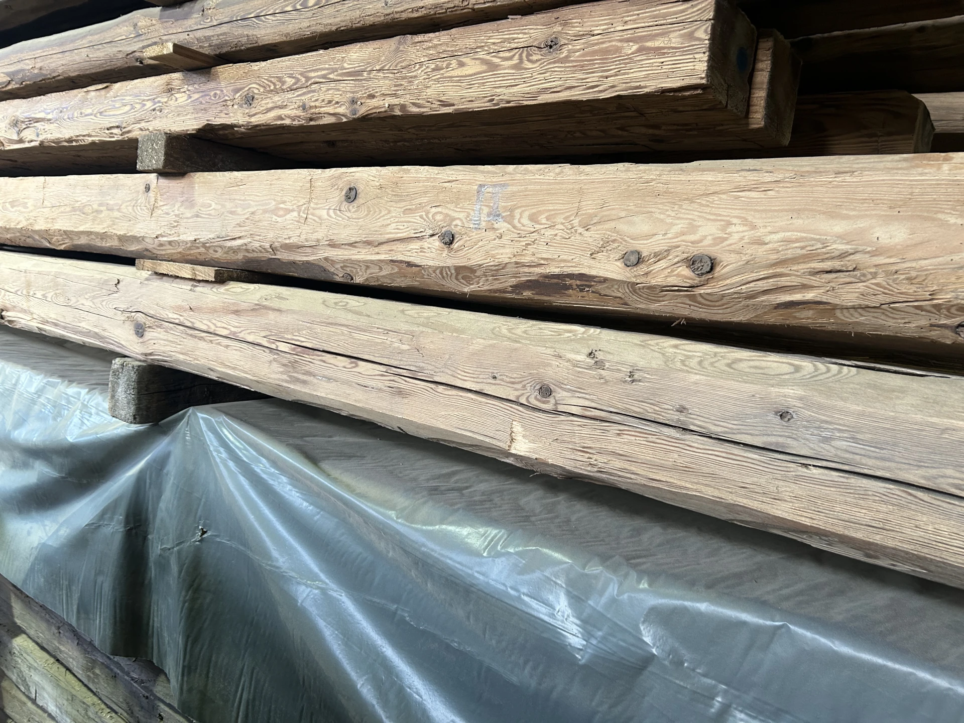 Extreme Nahaufnahme eines Stapels hochwertig aufbereiteter Kanthölzer, die die beilgehauene Oberfläche und die historische Patina zeigt.