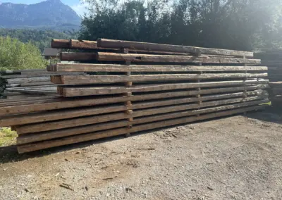 Seitliche Panoramaaufnahme eines großen Stapels langer Altholz-Sparren im Lager, die die gesamte Länge der Balken zeigt.