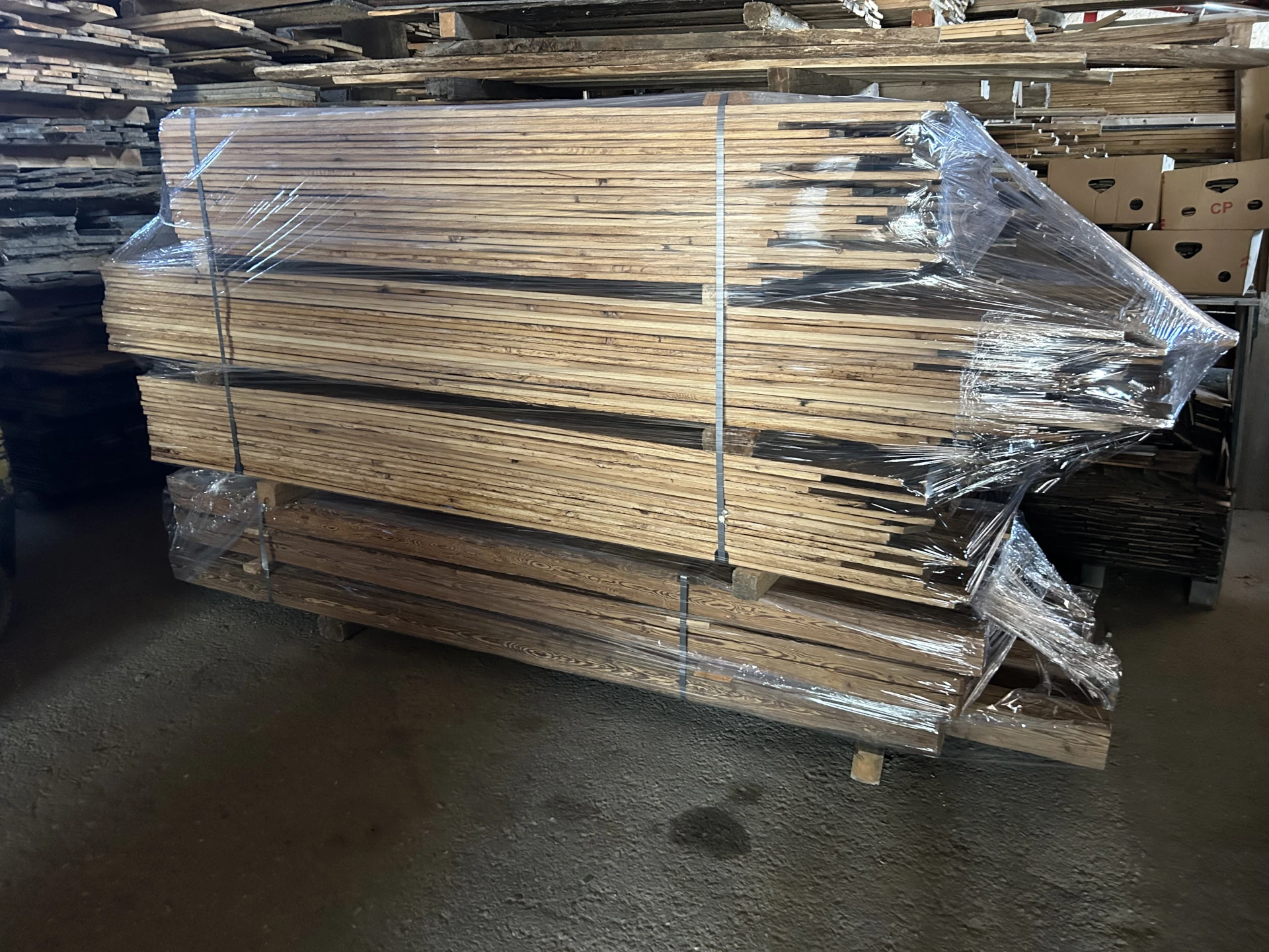 Transportfertig verpackter Stapel sonnenverbrannter Altholzbretter, sicher einfoliert für den Versand zum Kunden.