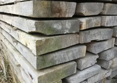 Ein großer Stapel Altholz-Dübelbäume im Lager, schräg fotografiert, sodass die breiten Querschnitte und die massiven Dimensionen gut sichtbar sind.