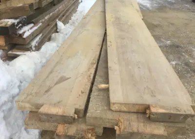 Ein kleiner Stapel roher, ungeschnittener Dübelbäume im Lager, die die typischen Merkmale alter Zwischendecken aufweisen.